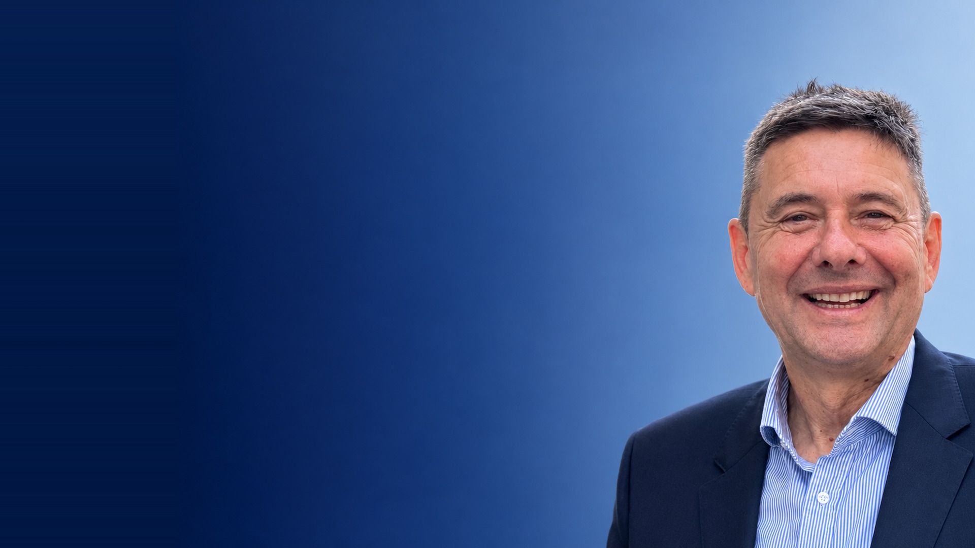 Matthias Ostendorff, Geschäftsführer der VERSINA Versicherungsmakler GmbH, lächelnd im Anzug vor blauem Hintergrund